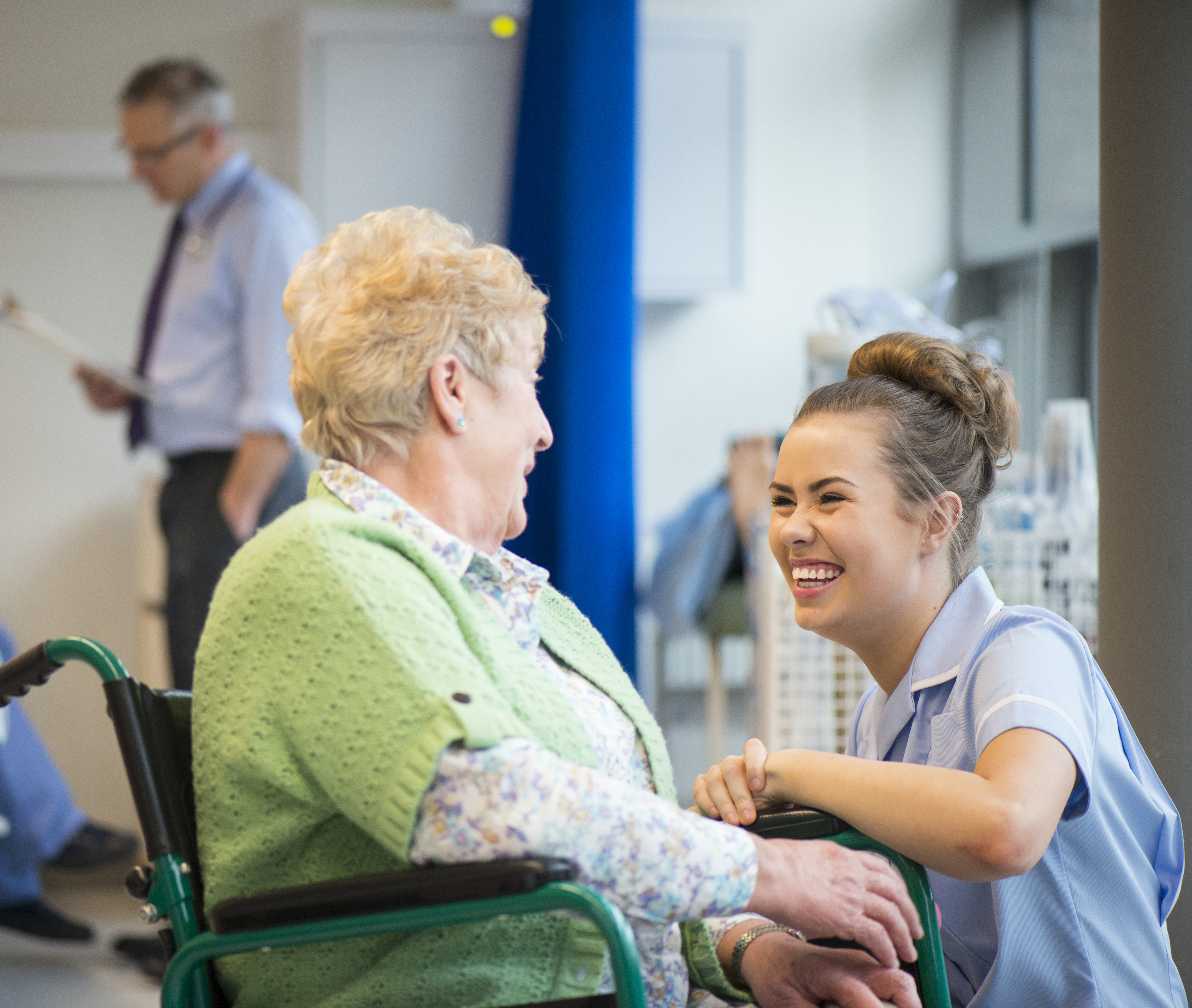 A hospital staff member speaking to a patient sat in a wheelchair