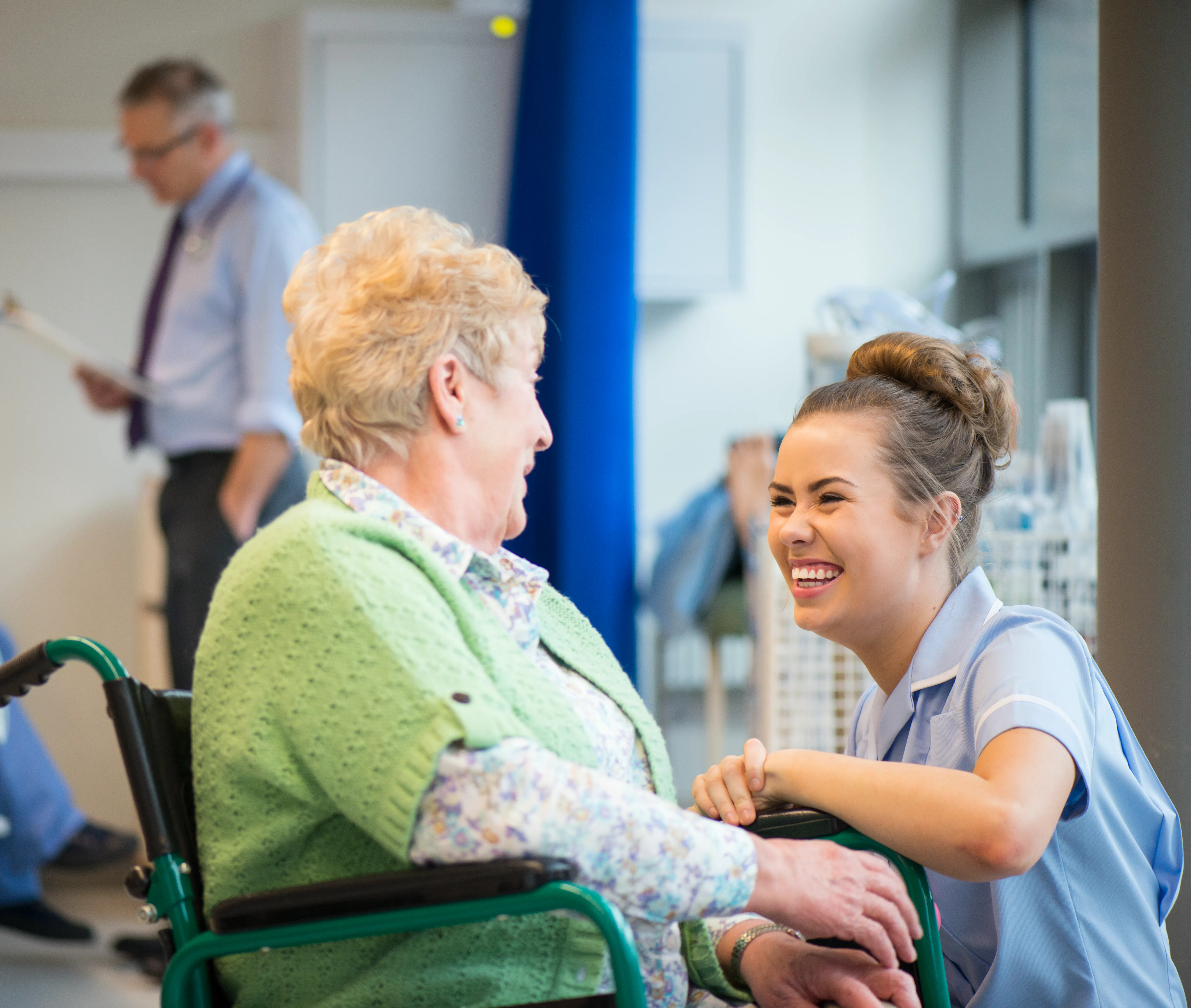 A hospital staff member speaking to a patient sat in a wheelchair